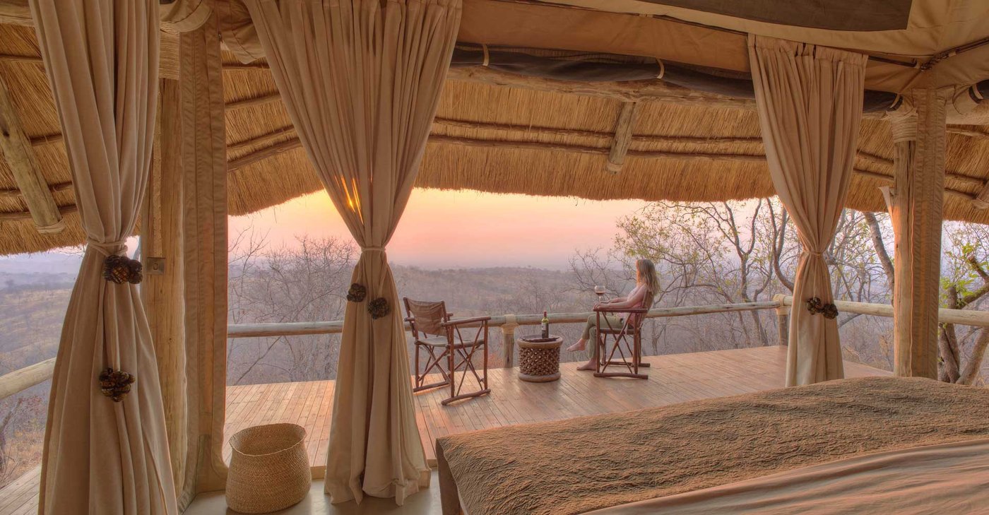 Tented bedroom with sheer curtains opening onto a valley-view deck at Ikuka Safari Camp