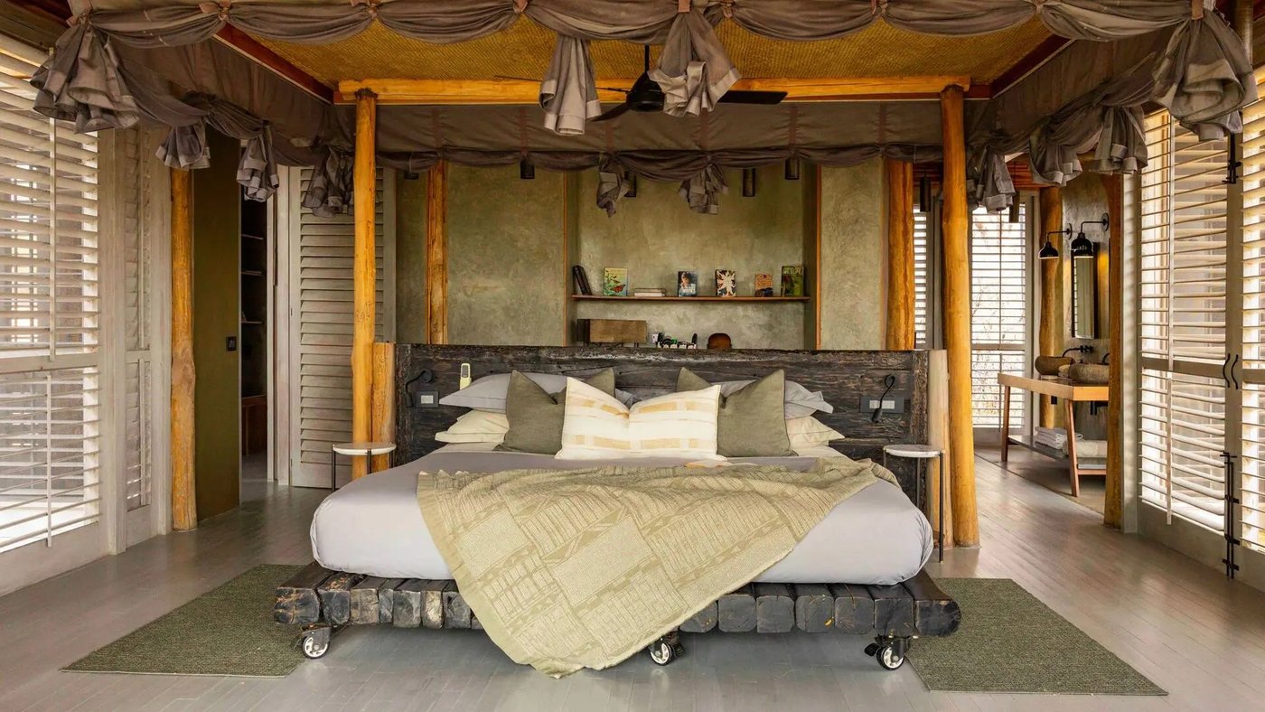 Canopied bed draped in fabric beneath rustic wood beams at Jabali Private House