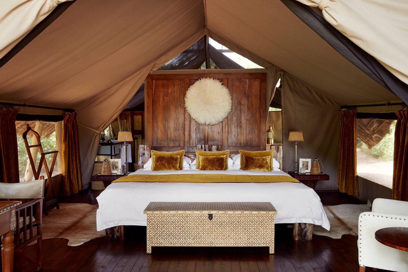 Tented bedroom with a carved wood headboard and warm gold tones at Jongomero Camp