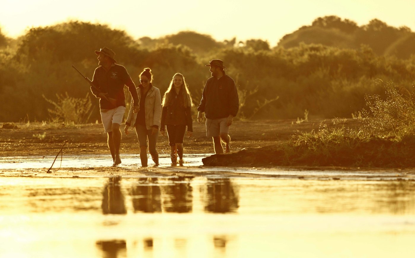 Walking safari group reflected in shallow water at sunset near Kichaka Expeditions