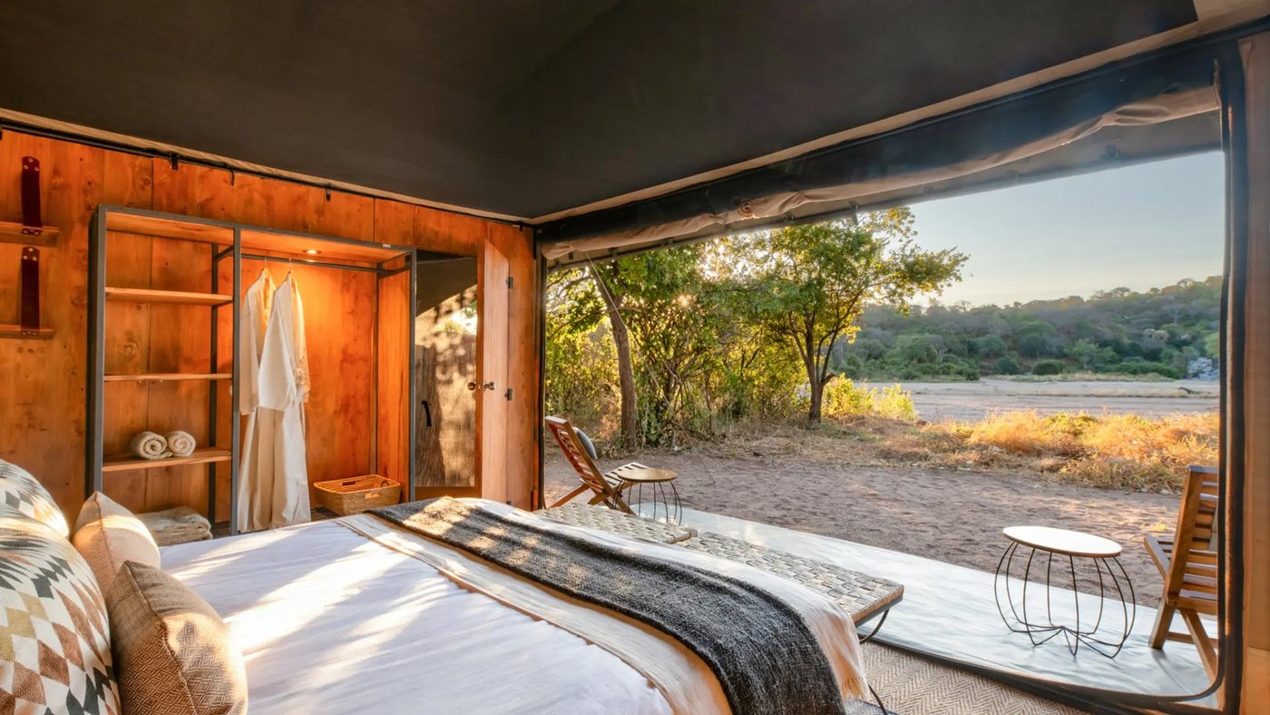 Open-sided tented bedroom with wooden shelving overlooking the river at Kokoko Camp