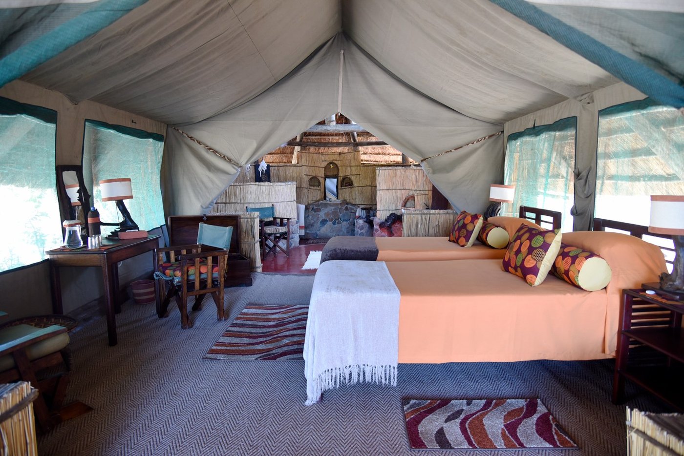 Tented bedroom with a warm orange bedspread and timber roof beams at Mwagusi Safari Camp