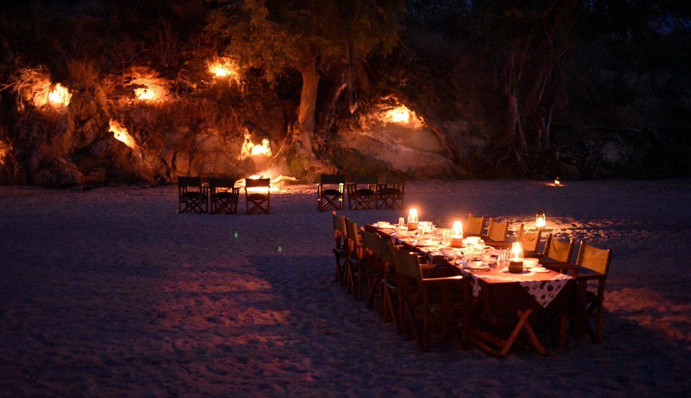 Candlelit bush dinner table set beneath a rock overhang at Mwagusi Safari Camp