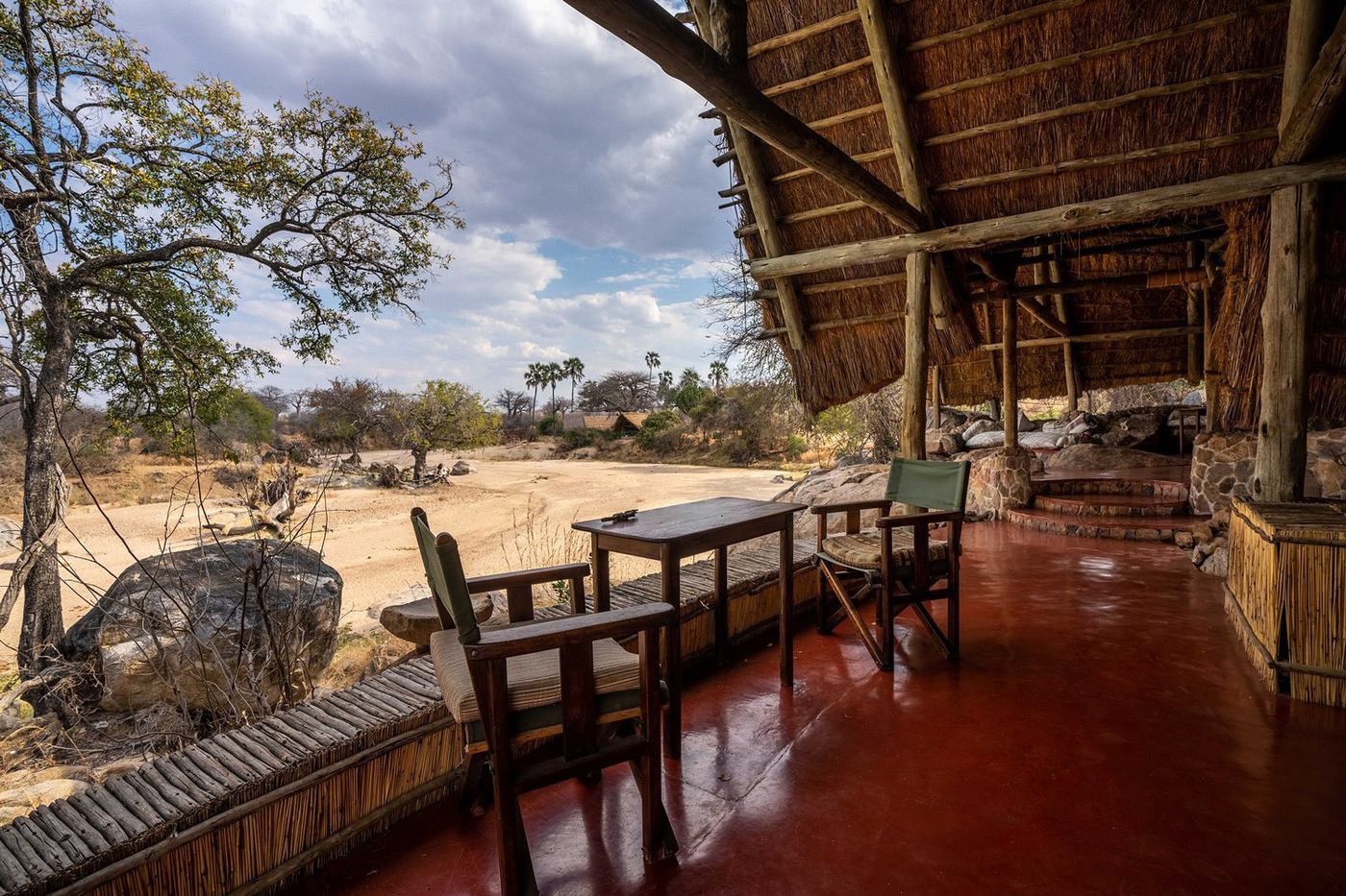Red-floored veranda with chairs overlooking the dry Mwagusi riverbed at Mwagusi Safari Camp