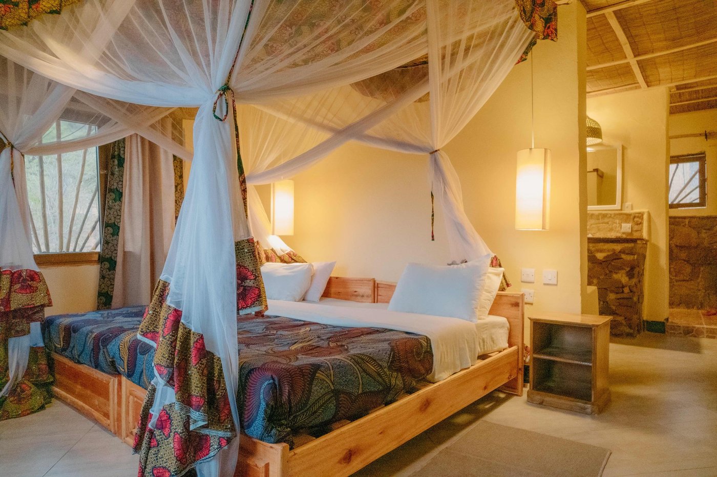 Bedroom with a mosquito net canopy and colorful Tanzanian textiles at Ruaha Hilltop Lodge