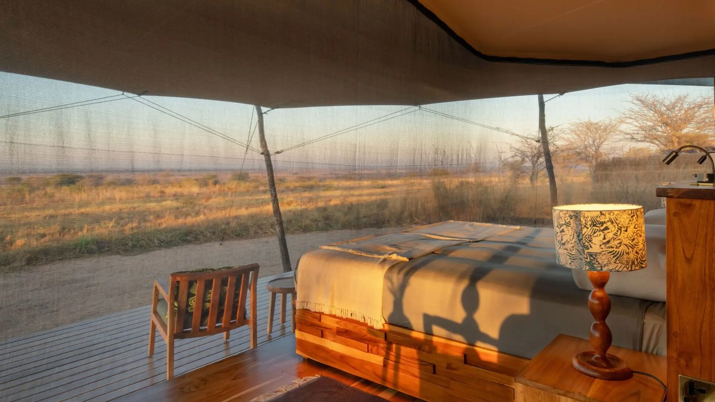 Tented bedroom bathed in sunset light with a private deck at Usangu Expedition Camp
